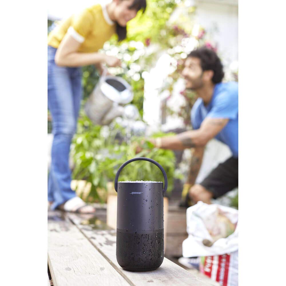 Black Bose speaker on a wooden surface with people gardening in the background