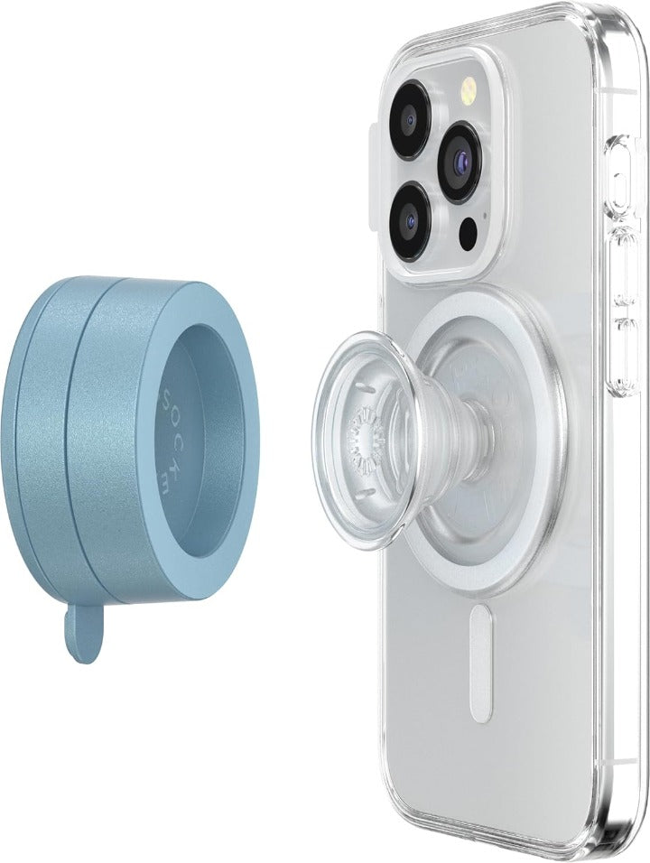 A smartphone with a clear case is shown with an attached clear PopSocket grip, and a blue sigh PopSockets Suction Mount for MagSafe positioned beside it. The phone's back displays the MagSafe alignment ring, highlighting its compatibility with MagSafe accessories. The blue sigh mount, shown separately, demonstrates its circular design and soft color. The clear PopSocket grip is expanded, illustrating its functionality for easy handling of the phone.