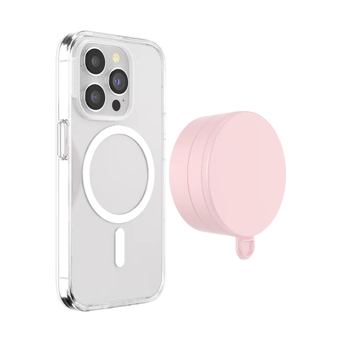 A smartphone with a clear case is shown next to a dusty rose PopSockets Suction Mount for MagSafe. The phone's back displays the MagSafe alignment ring, indicating its compatibility with MagSafe accessories. The mount is positioned beside the phone, highlighting its circular design and soft pink color. The clear case allows visibility of the phone's details and the MagSafe ring, emphasizing the mount's functional and stylish design.