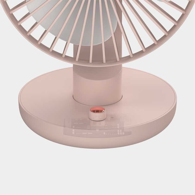Close-up of the base of a pastel pink desk fan with a minimalist design. The circular base features a small, metallic rose-gold power button and a smooth matte finish. The fan blades are enclosed in a sleek grille, and the background is plain white, emphasizing the fan's modern aesthetic.