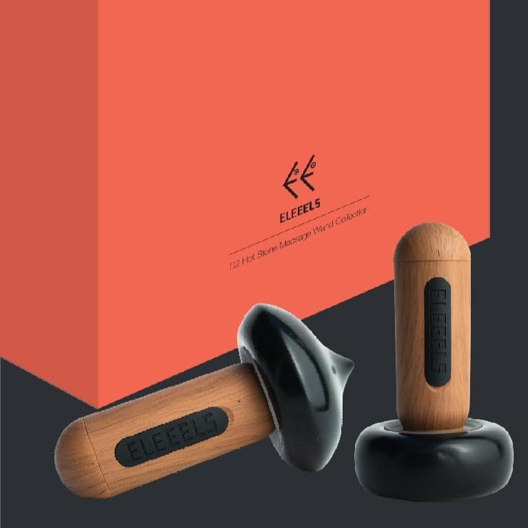 The ELEEELS S2 Hot Stone Massager is showcased alongside its sleek orange packaging. The device features a wooden handle with the "ELEEELS" logo and a black ergonomic base, designed for comfortable use. One device is upright on its base, while the other is tilted, highlighting its smooth, modern design. The minimalistic packaging complements the product's sophisticated aesthetic.