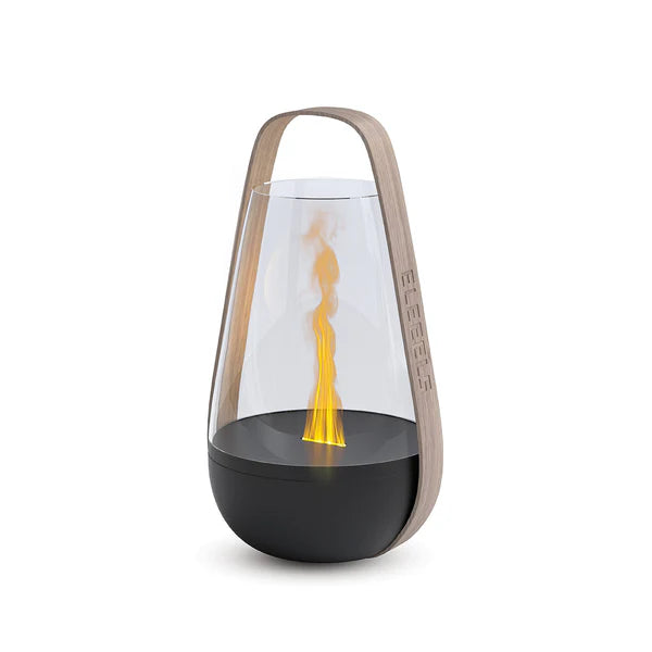 A modern flame-inspired ambient light featuring a sleek black base, a transparent glass enclosure, and a warm yellow-orange light resembling a flame. The design includes a natural wood-like handle engraved with the "ELEEELS" logo, adding portability and a minimalist aesthetic. The clean, elegant look makes it suitable for various settings.