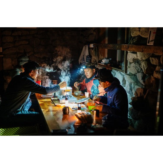 Group of people enjoying a meal in a dimly lit room, using headlamps to illuminate their surroundings, emphasizing the practicality of LED Lenser headlamps in low-light and outdoor settings.