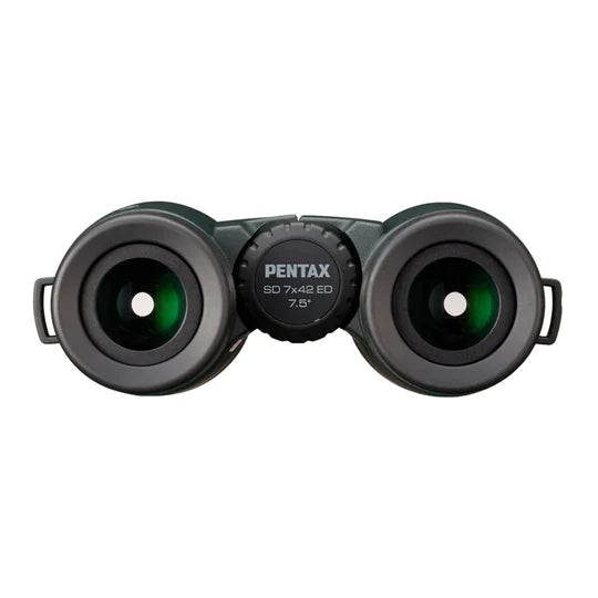 A front view of Pentax SD 7x42 ED binoculars showing the large objective lenses with a greenish tint. The central focusing wheel, labeled with "PENTAX SD 7x42 ED 7.5°," is prominently visible. The binoculars have a robust design with smooth surfaces for a comfortable grip. The eyecups are designed for ease of viewing, emphasizing durability and high-quality optics.