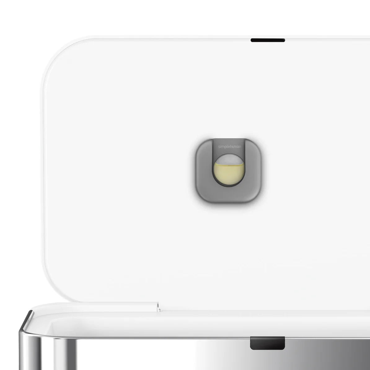 The image shows the interior of a Simplehuman trash can lid, finished in white. The lid is open, revealing a small circular compartment designed to hold an odor filter. This filter compartment is marked with the Simplehuman logo and is intended to house a replaceable carbon filter, which helps minimize odors inside the trash can. The design is sleek and minimalist, consistent with Simplehuman's modern aesthetic. The white finish adds to the clean and contemporary look, making this trash can both functional