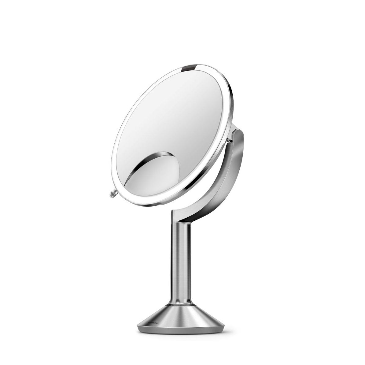 This is another angle of the **Simplehuman sensor mirror** with a pedestal stand. The mirror showcases a **side view**, highlighting its adjustable tilt mechanism, allowing users to position the mirror at their preferred angle. The chrome or brushed metal finish on the pedestal adds a sleek, modern look to the design. The **built-in LED lighting** ring ensures optimal illumination, and the smaller magnification mirror is visible for enhanced close-up details. This side view emphasizes the mirror's sturdy, e