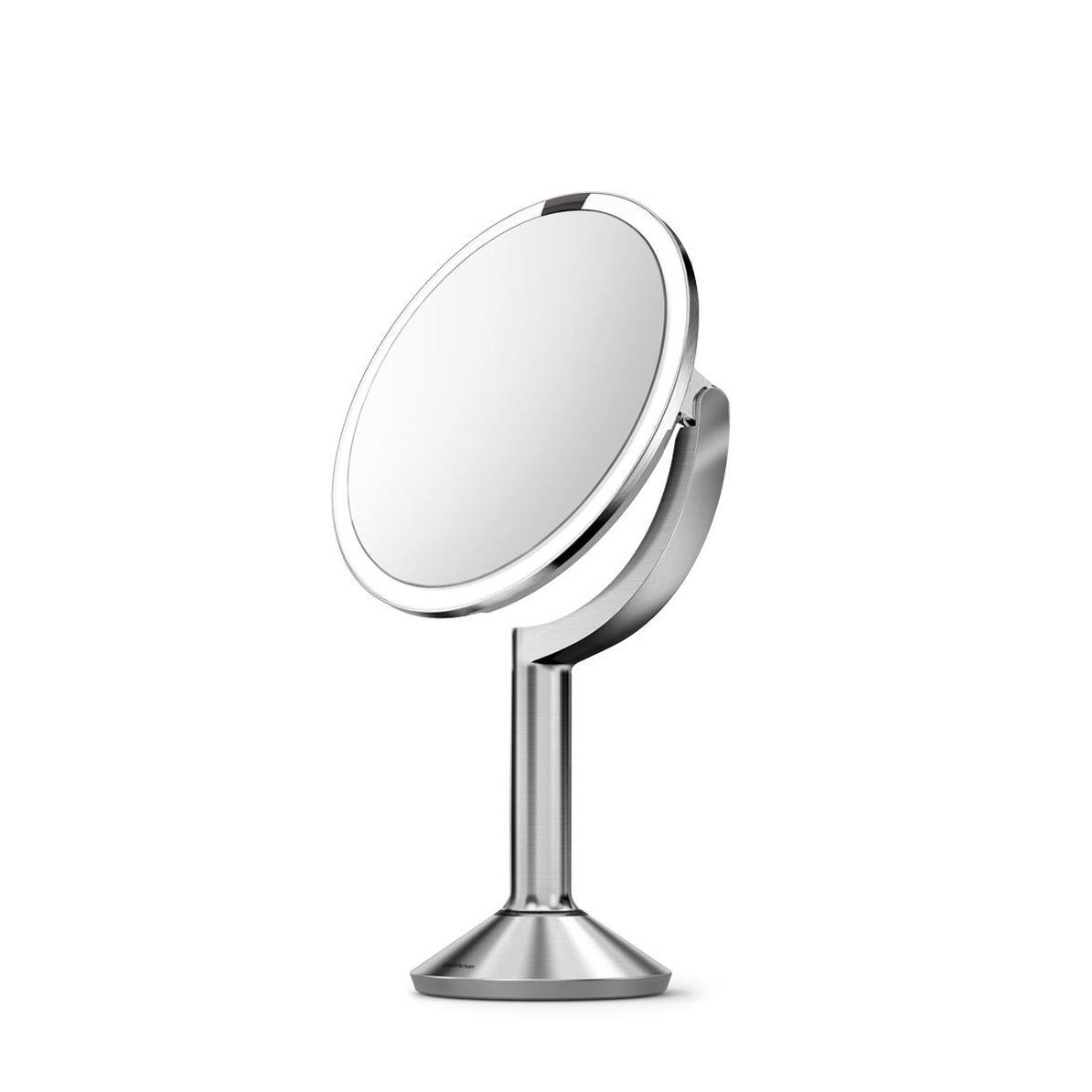 This is another angle of the **Simplehuman sensor mirror** in a chrome or brushed metal finish. The mirror features a **sleek pedestal stand** and adjustable mirror head, allowing for customizable angles. Its **LED lighting ring** ensures bright, natural light for grooming and makeup application. The minimalist, modern design complements any vanity or bathroom setup, and the mirror's high-quality materials ensure durability and elegance. This image captures the mirror's refined aesthetic and functional desi