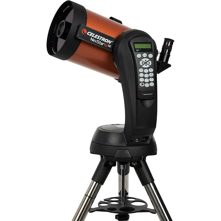  A Celestron NexStar 6SE telescope with an orange cylindrical tube mounted on a black computerized base and a silver tripod. The telescope is angled slightly upward for observation. The base features a control panel with a keypad and a small display screen for navigation and settings.