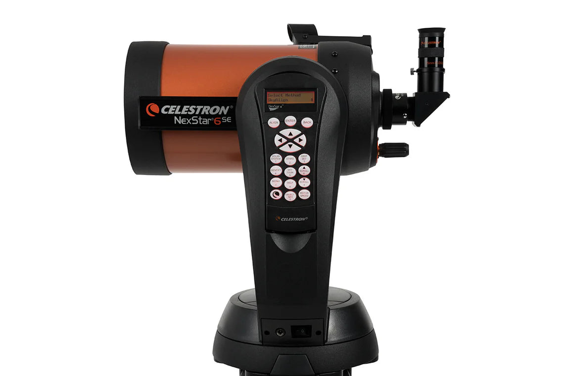A side view of a Celestron NexStar 6SE telescope with an orange cylindrical tube mounted on a black computerized base. The base features a control panel with a keypad and a small display screen for navigation and settings. The eyepiece is attached to the back of the telescope tube.