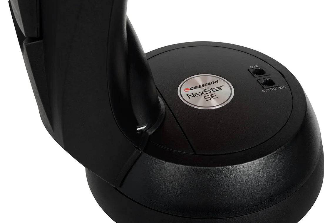  A close-up view of the Celestron NexStar SE telescope's base, showing the Celestron branding and the model name "NexStar SE" on a circular metal plate. The black, sturdy design of the base is visible, highlighting the robust construction and attention to detail in the telescope's build.