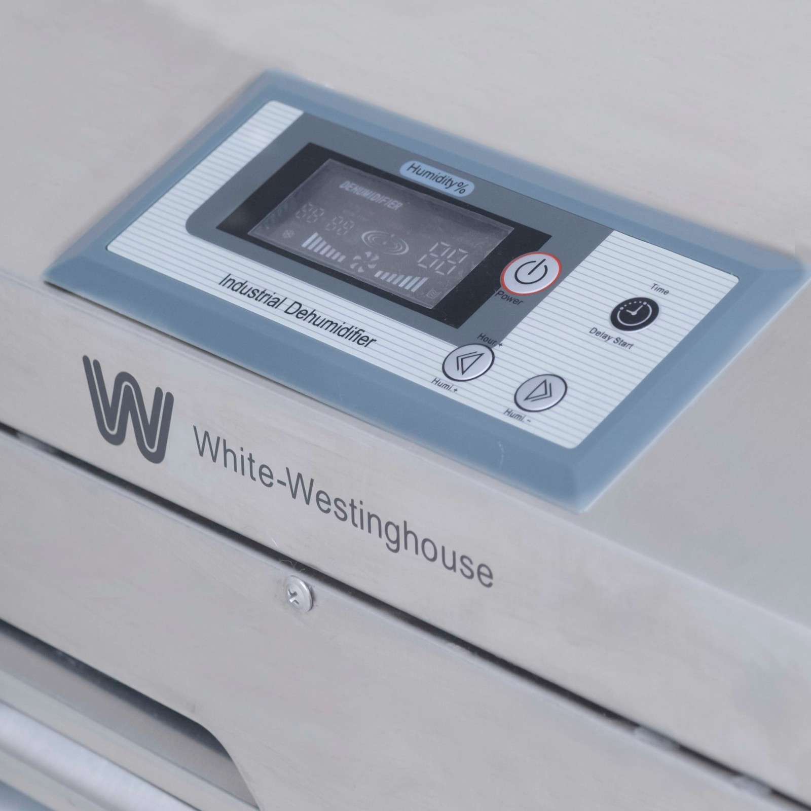 A close-up view of the control panel on a White-Westinghouse industrial dehumidifier. The panel includes an LCD display showing various settings and humidity levels. There are labeled buttons for "Power On/Off" with a red circle, "Timer" with a clock icon, and two arrow buttons labeled "Add" and "Minus" for adjusting settings. The branding "White-Westinghouse" is visible below the control panel on the metallic silver exterior of the dehumidifier.