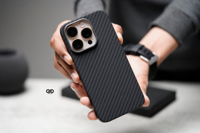 This image shows a person holding a sleek phone case with a carbon fiber texture, providing a minimalist and sophisticated look. The case features a cutout for a multi-lens camera setup, suitable for higher-end smartphones with triple-lens cameras, possibly a recent model from Apple's iPhone series. The carbon fiber pattern not only adds a refined aesthetic but also likely offers a sturdy grip and enhanced durability for everyday use. The design emphasizes both style and functionality, appealing to users lo