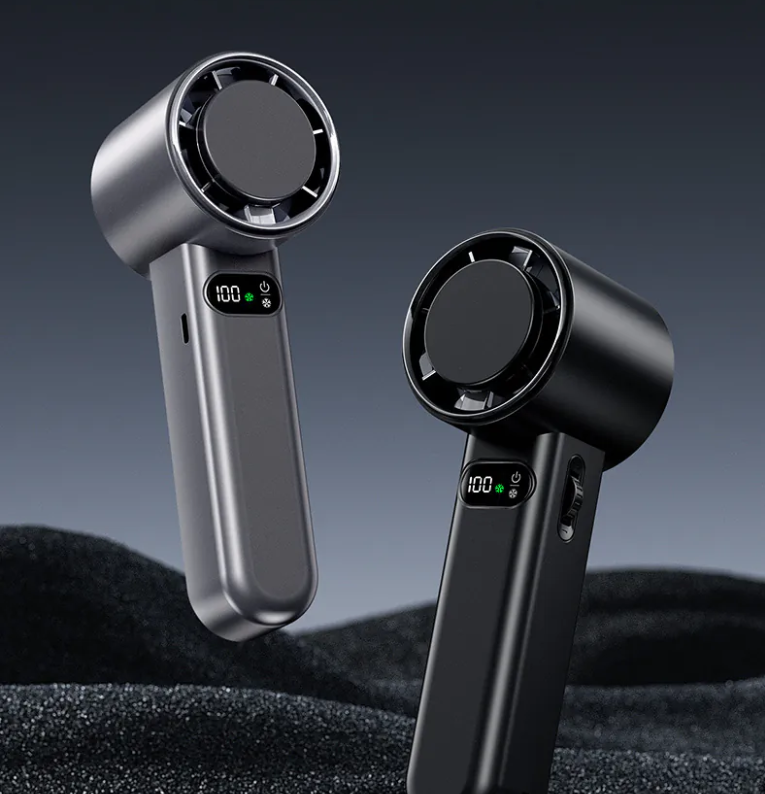 Two sleek handheld portable fans, one in metallic gray and the other in matte black, displayed against a textured dark surface with a gradient gray background. Each fan features a compact, circular front grille and an integrated digital display showing "100%" battery life alongside icons for speed and power. The designs include smooth, ergonomic handles with side controls for functionality.