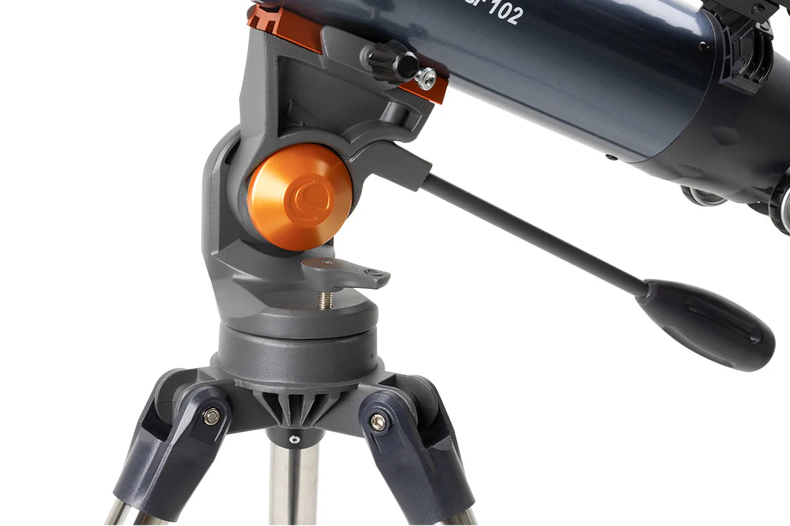 A close-up view of the mount and control handle of a Celestron AstroMaster 102 telescope. The mount is gray with an orange adjustment knob, providing a secure and stable connection to the tripod