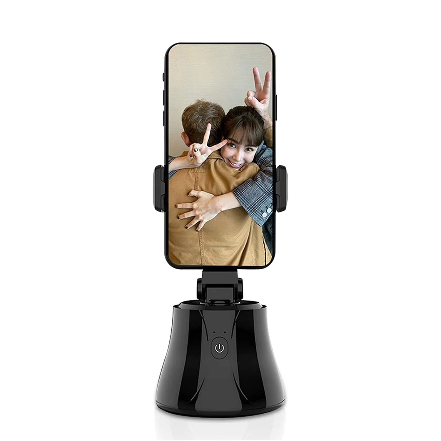 A smart selfie stick with a smartphone mounted on it, showing a photo of two people hugging and smiling, with one person giving a peace sign. The device has a sleek black base with a power button on the front and securely holds the phone in place.