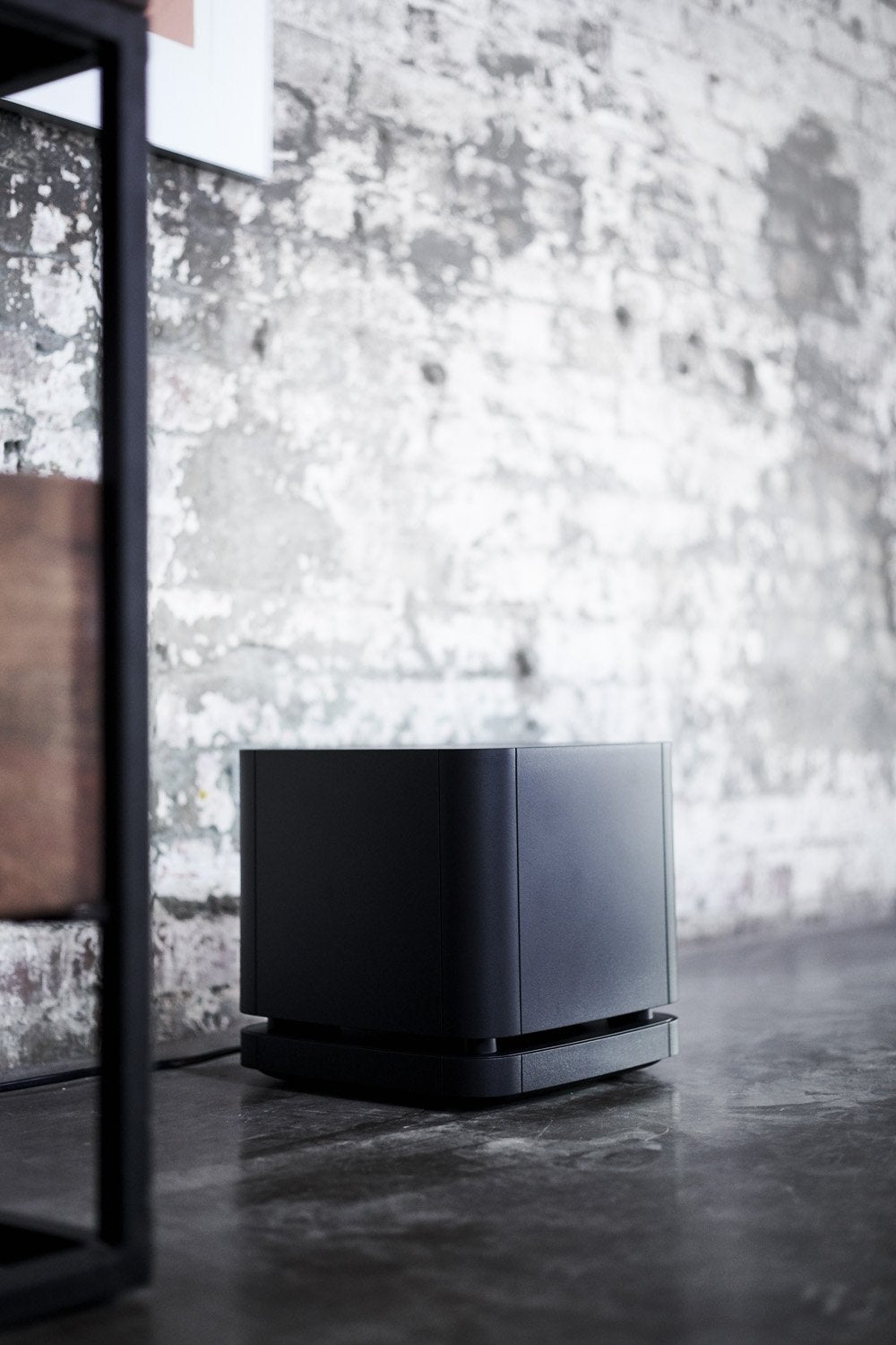 Black subwoofer on a dark surface with a textured wall background