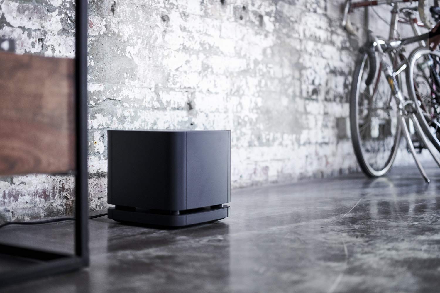 Black electronic device on a concrete floor with a brick wall and bicycle in the background