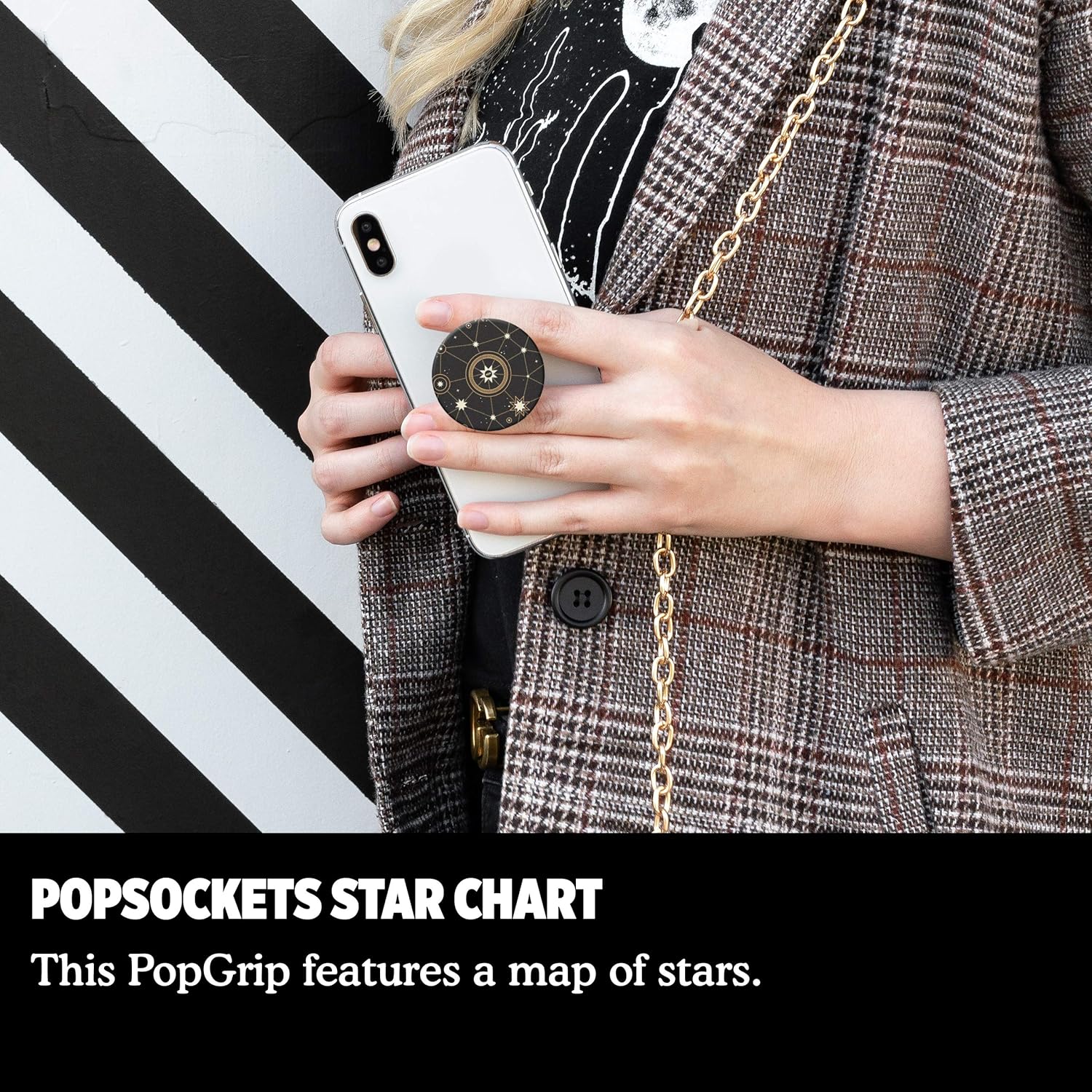 A person wearing a plaid blazer is holding a white phone with a PopSockets grip featuring a star chart design. The person has a chain strap over their shoulder.