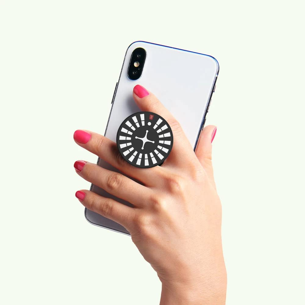 A hand holding a smartphone with a PopSockets Backspin Roulette grip attached to the back. The grip has a black circular top with white segments arranged like a roulette wheel, featuring a red segment marked with the number "7" and a white cross-like shape in the center. The person holding the phone has pink nail polish, and the grip is expanded, allowing for a secure hold.