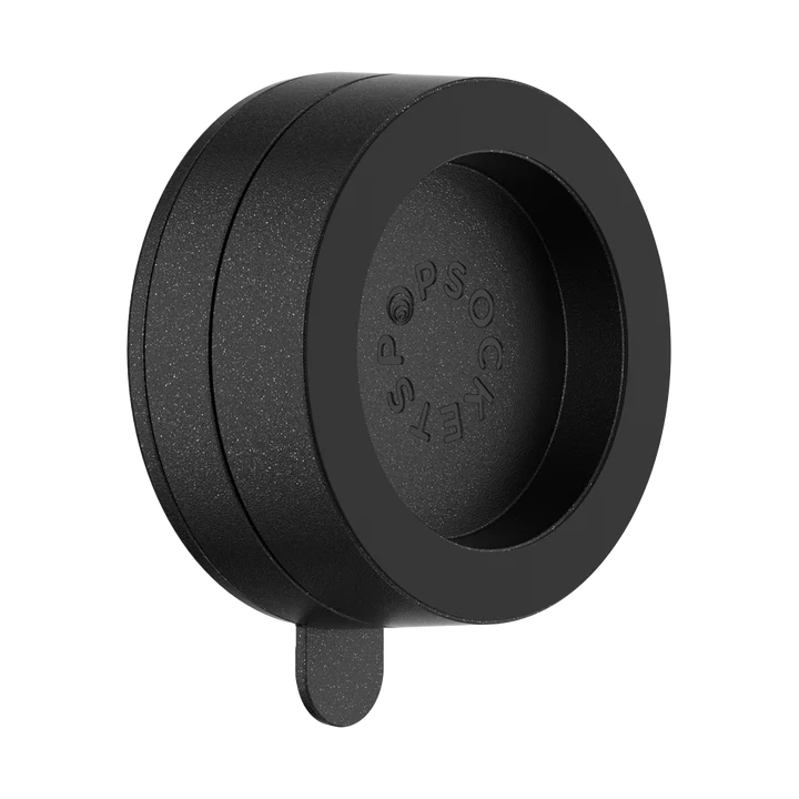 A PopSockets Suction Mount for MagSafe in black is shown against a plain background. The mount has a circular design with the PopSockets logo embossed on the inner surface. A small tab extends from the bottom, likely for easy removal or adjustment. The sleek black finish emphasizes the mount's minimalist and functional design.