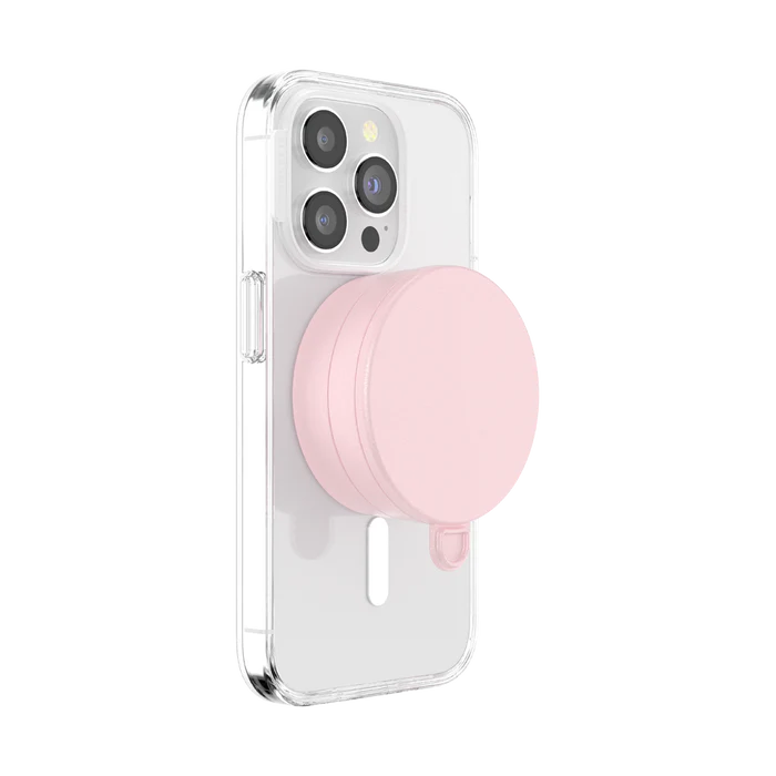 A smartphone with a clear case is shown with a dusty rose PopSockets Suction Mount for MagSafe attached to its back. The mount is securely positioned in the center of the phone's back, demonstrating its compatibility and ease of use with MagSafe technology. The phone's camera lenses are visible at the top, emphasizing the mount's unobtrusive and stylish design.