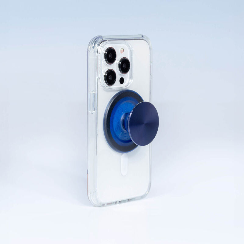 A smartphone with a clear case is shown with a French Navy PopGrip for MagSafe attached to its back. The PopGrip is extended, showcasing its functional grip, with a glossy, slightly reflective navy blue surface. The phone's camera lenses are visible at the top, highlighting the PopGrip's sleek and modern design, which complements the phone's aesthetics while providing a practical grip for easier handling