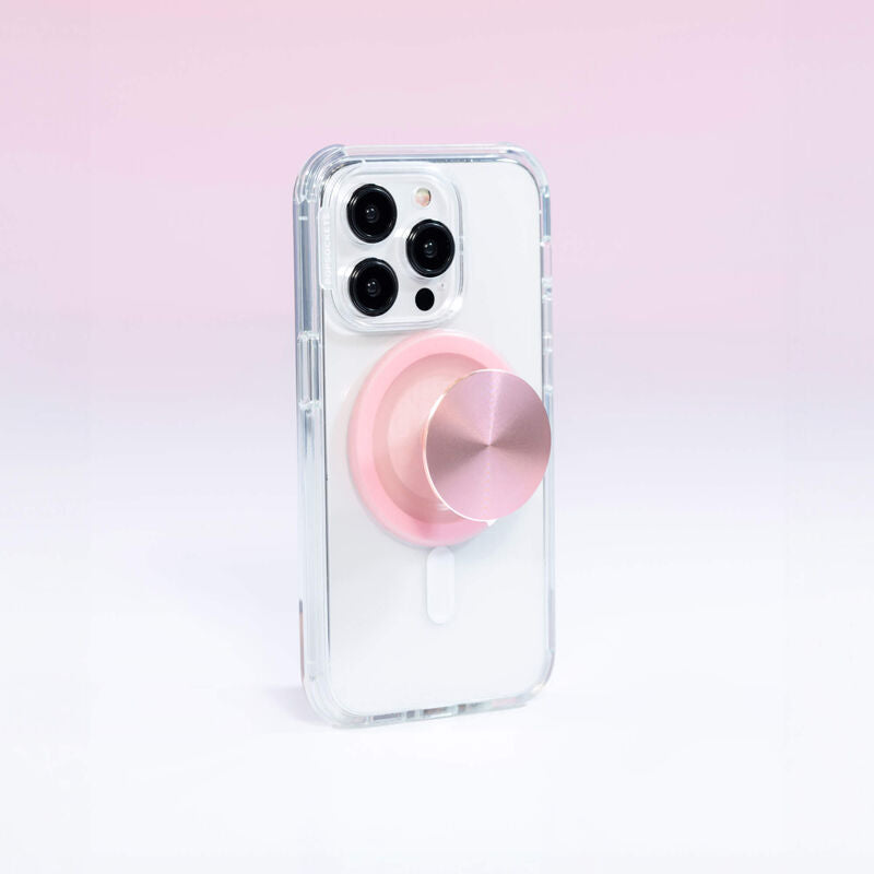 A smartphone with a clear case is shown with a PopSockets MagSafe PopGrip in dusty rose color attached to its back. The PopGrip is extended, showcasing its functional grip, with a glossy, slightly reflective soft pink surface. The phone's camera lenses are visible at the top, highlighting the PopGrip's sleek and modern design, which complements the phone's aesthetics while providing a practical grip for easier handling.