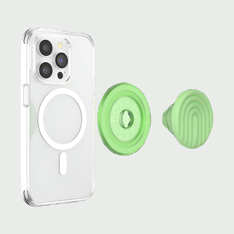 A clear phone case with a MagSafe ring is shown beside a detached PopOut Curves Matcha Dew PopGrip for MagSafe. The PopGrip features a light green color with curved lines, ready to be attached to the phone case, providing a secure and stylish grip for the device