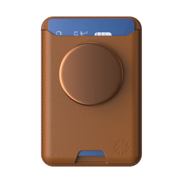 PopSockets MagSafe Softgoods PopWallet in Cognac, viewed from the front. The wallet holds a blue card, partially visible at the top. The cognac-colored circular PopSocket is centered on the wallet's body. The wallet has a smooth, leather-like texture with precise stitching along the edges. The PopSockets logo is embossed near the bottom right corner.