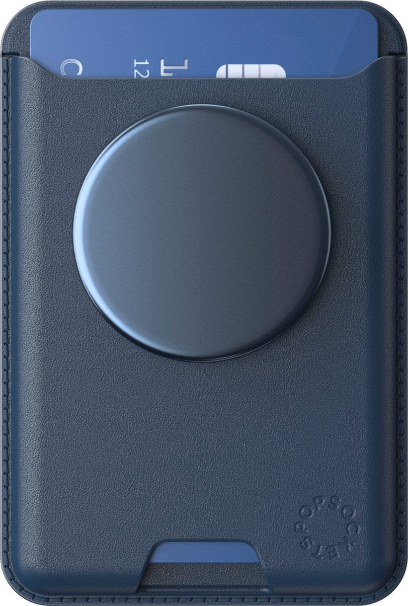 A close-up of a navy blue leather PopSockets MagSafe Softgoods PopWallet. The wallet is attached to a phone and has a circular PopSocket on the back. A blue card is partially inserted into the card slot, showcasing the wallet's functionality and sleek design. The texture of the leather and subtle branding on the lower right corner are visible.