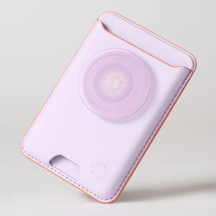 A close-up view of the PopSockets MagSafe Softgoods PopWallet in Pale Lavender. The wallet is shown without a phone, emphasizing its design and texture. The lavender wallet features a circular PopSocket in the same color, positioned centrally. The PopSockets logo is embossed near the bottom right corner. The edges of the wallet are stitched, showcasing an orange accent along the sides. The top opening of the wallet is visible, designed to hold cards securely.