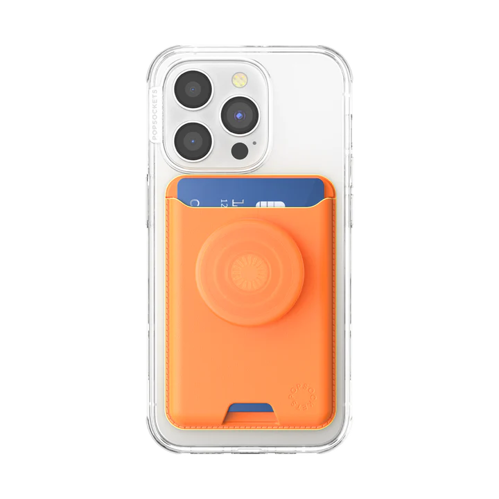 The back view of an iPhone with a clear case shows a Softgoods PopWallet for MagSafe in a bright cantaloupe color attached to it. The PopWallet has a matching cantaloupe PopGrip for easy handling. A blue credit card is partially visible, inserted into the PopWallet's card slot. The setup emphasizes the practical and stylish design of the PopWallet when used with a phone.