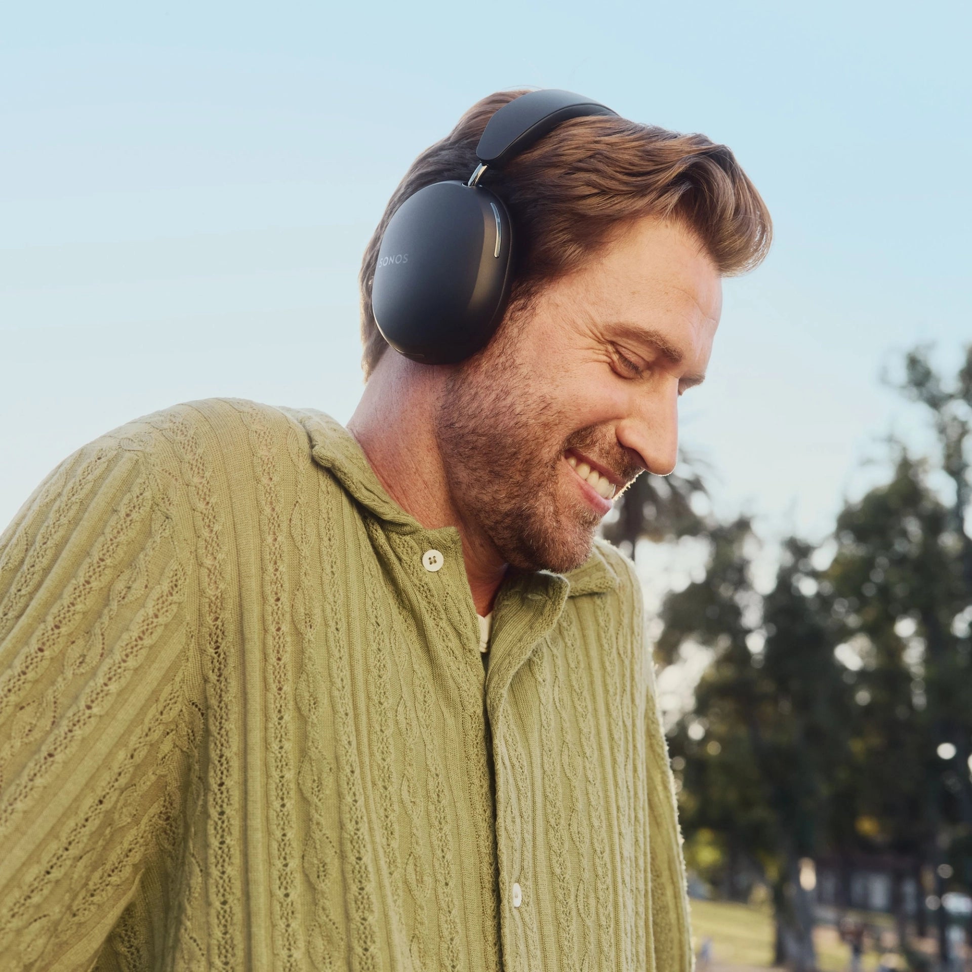 Man wearing black Sonos wireless over-ear headphones, enjoying music outdoors, highlighting comfort and sleek design.