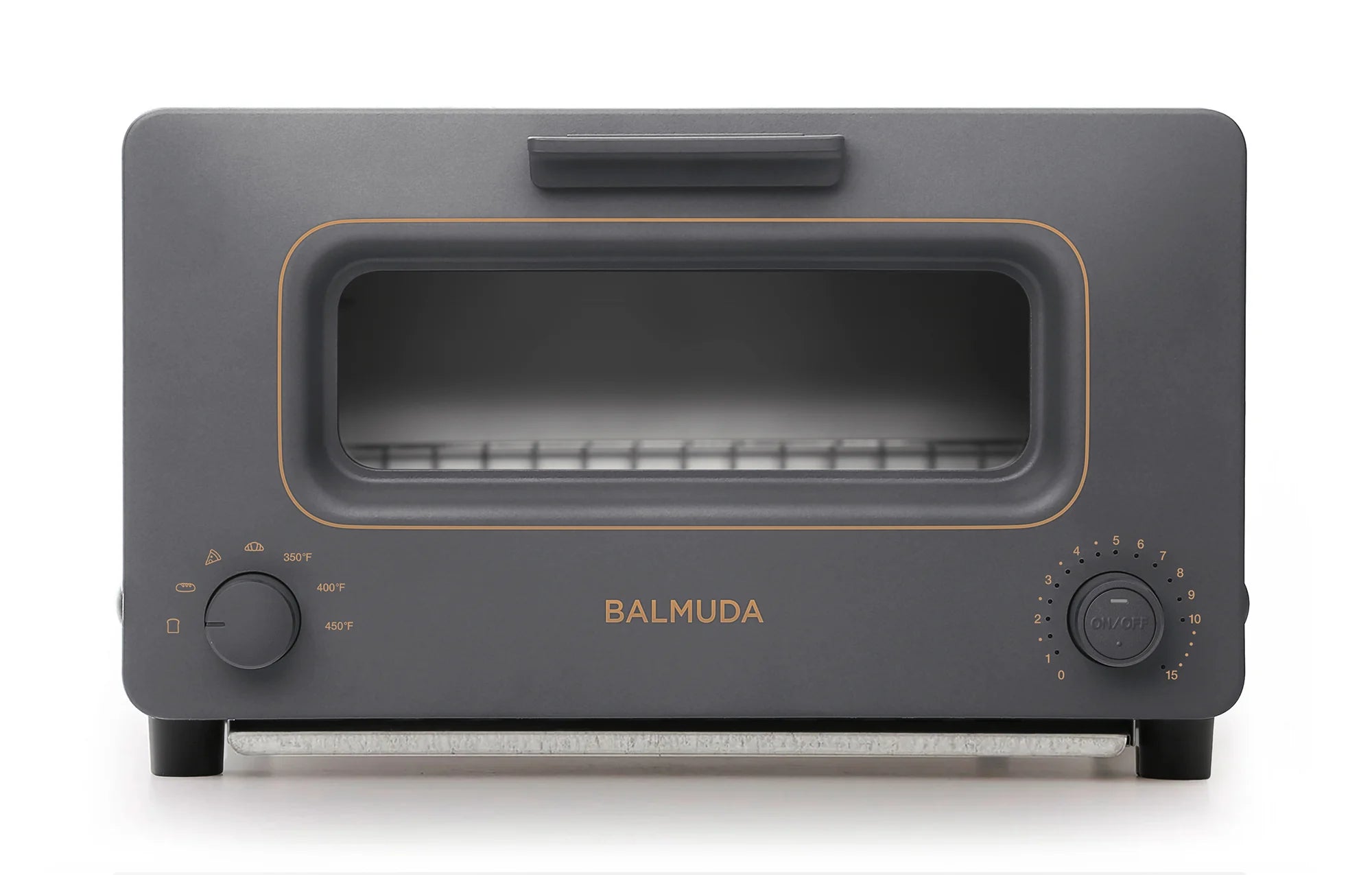 The image shows a front view of the Balmuda toaster in a matte dark gray finish with gold accents. The toaster features a large rectangular viewing window, bordered by a subtle gold accent. The brand name "BALMUDA" is centered below the window in matching gold lettering.