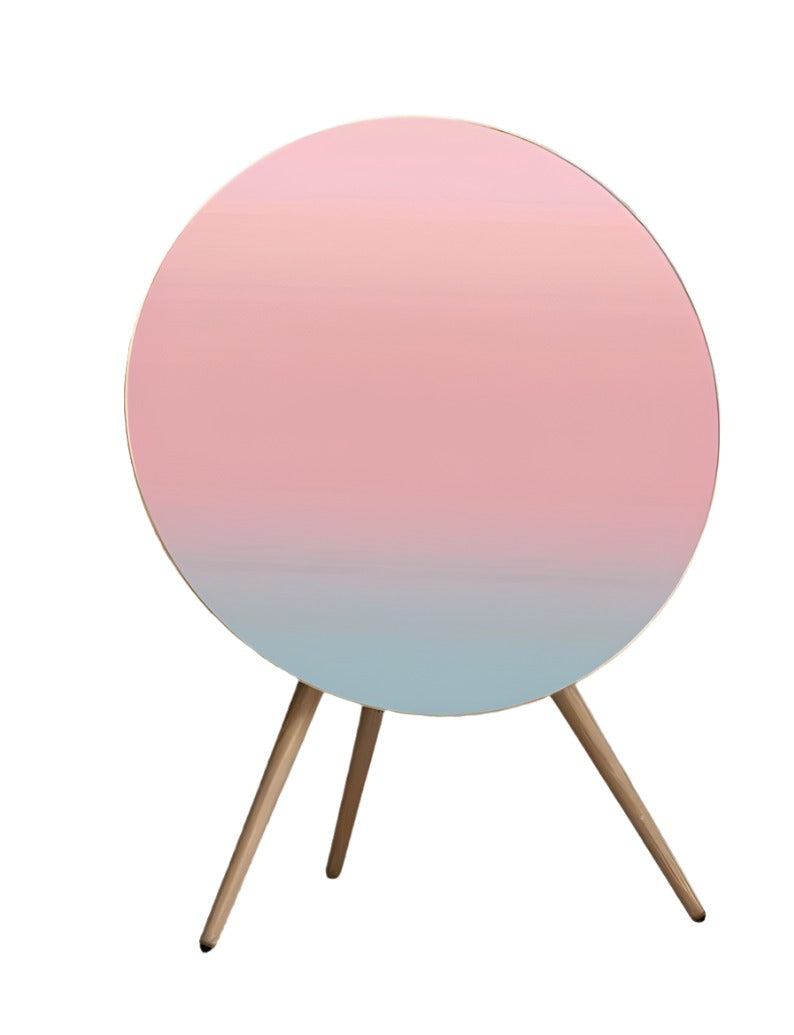 Bang & Olufsen speaker with a skin cover featuring a Coral Pink design, displaying a gradient pattern transitioning from soft pink at the top to a light blue at the bottom, mounted on a tripod stand.