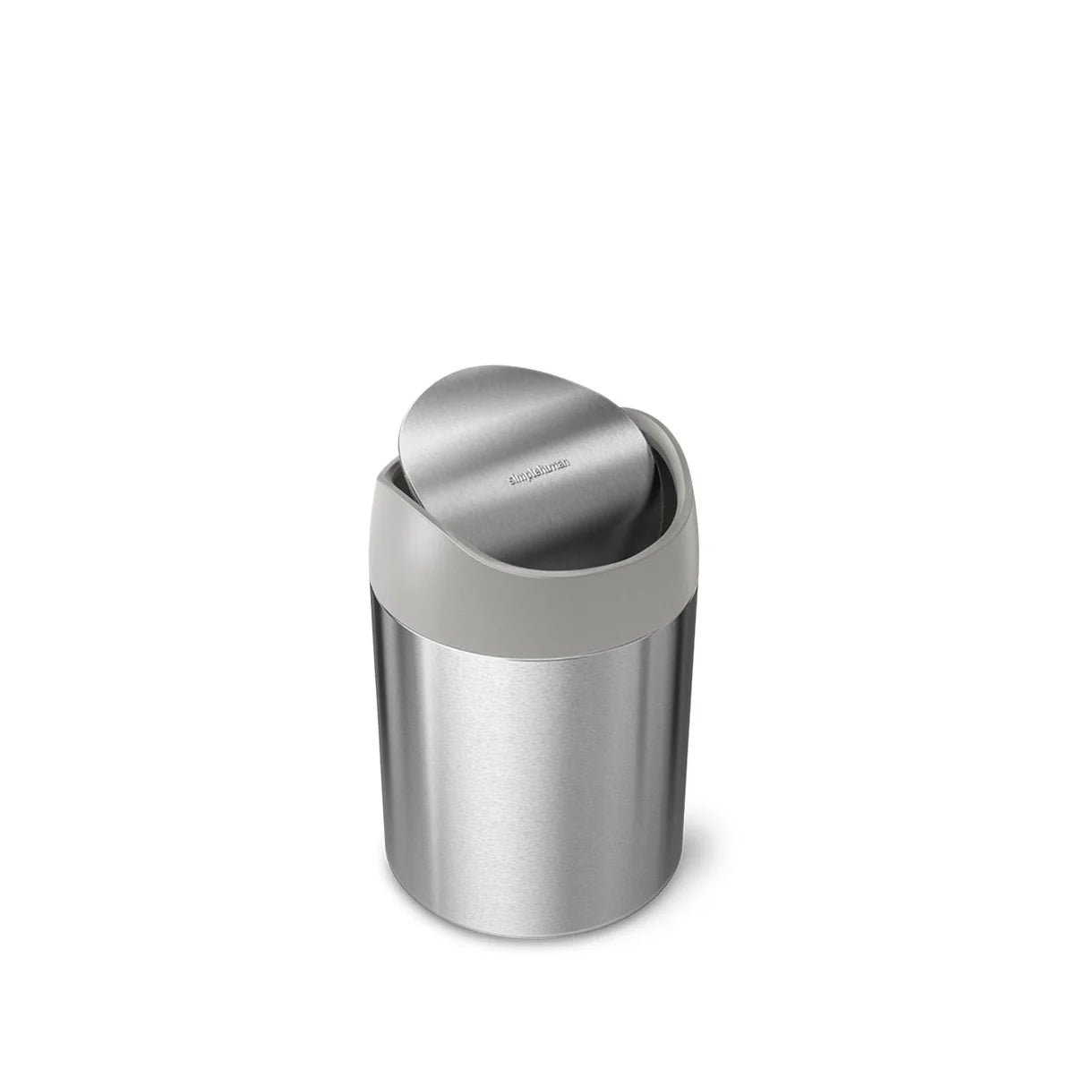 The image shows a Simplehuman mini round stainless steel trash can with a swing lid. The trash can is compact and cylindrical, making it ideal for use on a bathroom countertop, vanity, or desk. The body of the trash can is made of brushed stainless steel, giving it a sleek and modern appearance. The lid is a matte gray plastic swing-top, designed to easily open and close as items are disposed of. The swing lid has the Simplehuman logo subtly embossed on it, adding a touch of branding to the minimalist desig