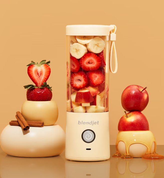 BlendJet 2 portable blender in a beige design, filled with strawberries, bananas, and apples, placed next to cinnamon sticks and honey-covered apples.