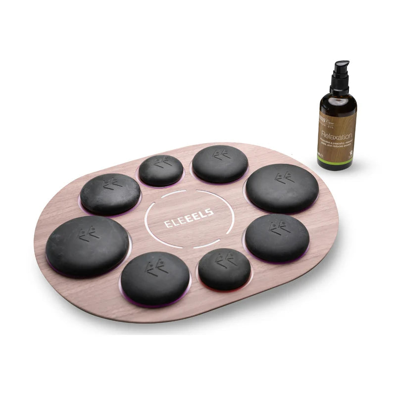 An ELEEELS hot stone therapy set featuring a sleek wooden oval tray with engraved slots perfectly holding smooth black stones marked with the ELEEELS logo. The setup includes a bottle of ELEEELS Care Relaxation Massage Oil placed nearby, highlighting the set's premium design for relaxation and wellness purposes.