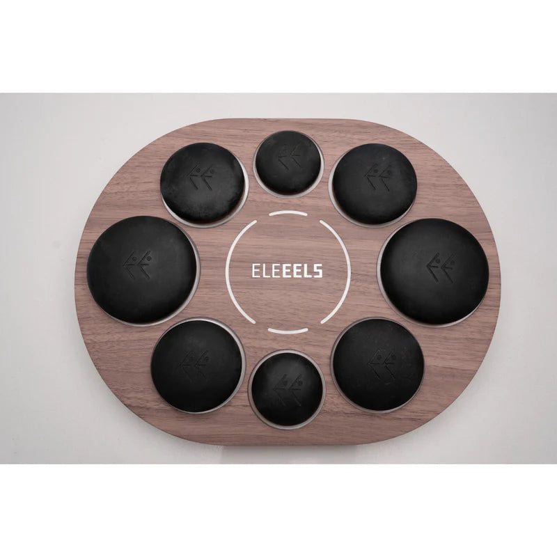A set of ELEEELS branded black hot stones arranged on a wooden oval tray with recessed slots to hold the stones securely. The tray features the ELEEELS logo in the center, surrounded by decorative white circular lines, emphasizing a sleek and organized design for therapeutic or relaxation purposes.