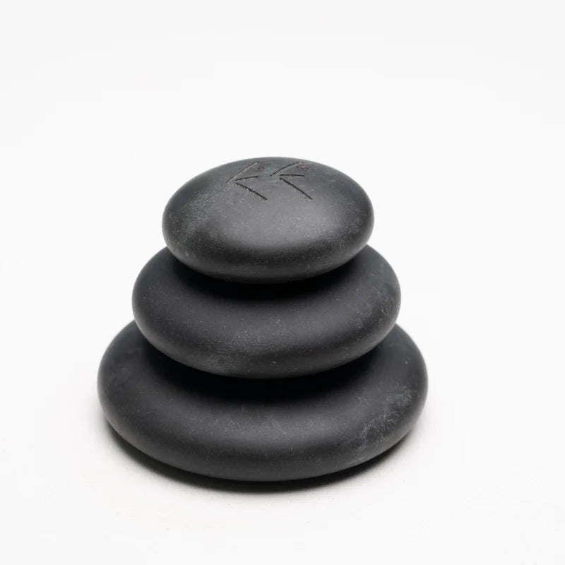 A stack of three smooth, black hot stones of varying sizes, with the ELEEELS logo engraved on the top stone. The stones have a polished finish, designed for use in therapeutic or relaxation treatments, emphasizing a natural and minimalist aesthetic.