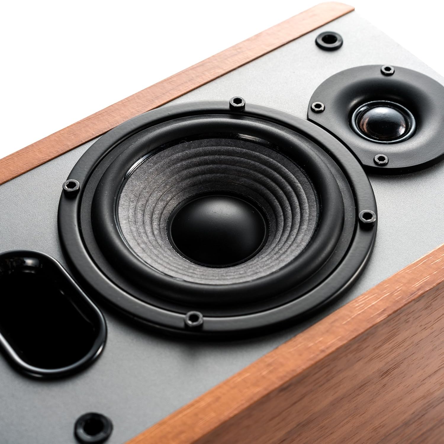 A close-up of a speaker showcasing its woofer, tweeter, and bass reflex port, set in a wooden enclosure with a polished finish, highlighting its craftsmanship and audio components.