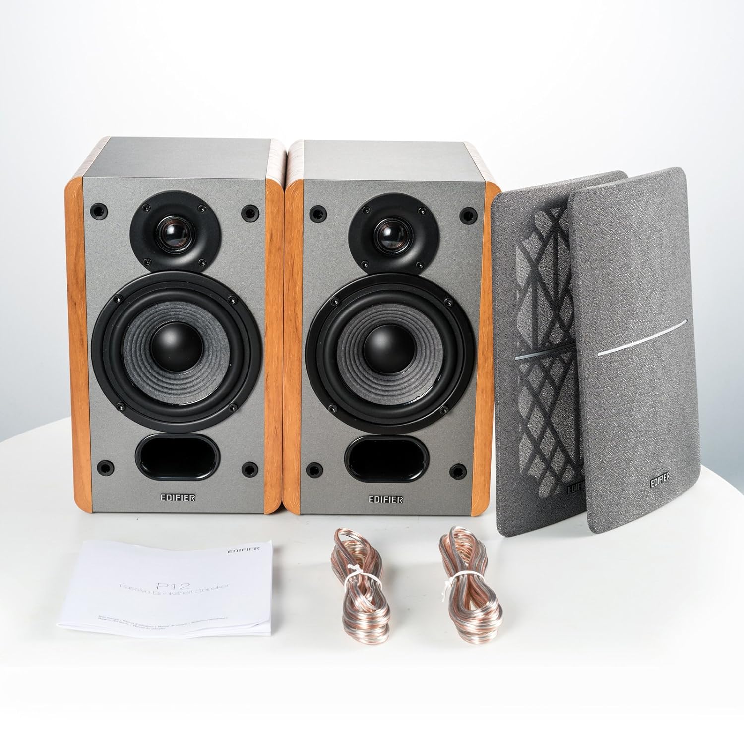 A set of bookshelf speakers with a gray front, wooden sides, removable grilles, speaker cables, and a user manual for easy setup and use.