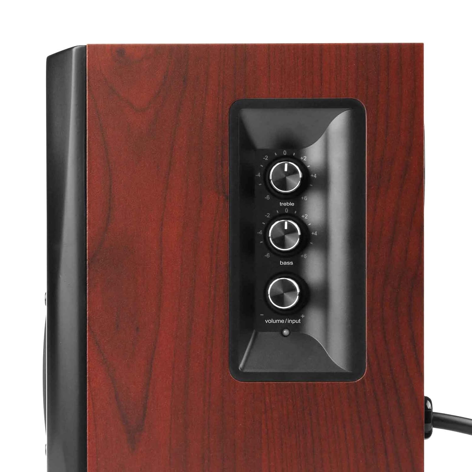 A close-up of a wooden speaker with a side panel featuring three black rotary control knobs. The top knob is labeled "treble," the middle one "bass," and the bottom one "volume/input." The side panel is surrounded by a glossy black border contrasting with the rich wood grain finish of the speaker. A power cable extends from the right side of the speaker.