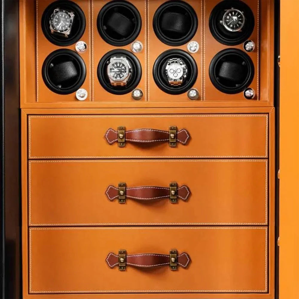 A watch storage unit features three orange drawers with brown leather handles. Above the drawers, there are eight circular compartments for holding watches, each containing a watch in a black holder. The unit is designed to securely store and display watches.