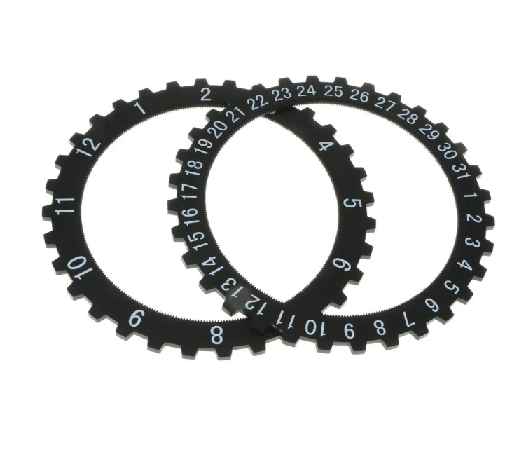 Three black gear-like clock rings with white numerals, displaying a combination of hour and date markings. The overlapping design showcases a mechanical or industrial clock component layout.