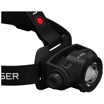  A close-up view of a black LED Lenser headlamp, focusing on the adjustable strap and the headlamp unit. The LED Lenser logo is visible on the strap. The headlamp features a prominent central light with an adjustable focus ring and a sturdy mount, highlighting its durable and practical design. The background is white, emphasizing the details of the headlamp.