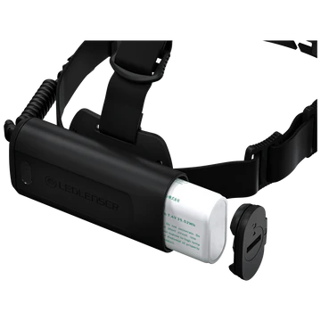 A close-up view of the battery compartment of a LED Lenser headlamp. The compartment is open, showing a white rechargeable battery partially inserted. The black adjustable strap is attached to the battery compartment, which features the "LED LENSER" branding. The end cap of the battery compartment is removed and positioned nearby, displaying the secure locking mechanism.