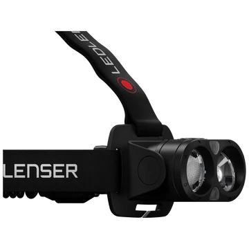 A close-up side view of an LED Lenser headlamp, showing the adjustable black strap with the "LED LENSER" branding. The light unit is attached to the strap and features dual clear lenses. The design highlights the headlamp's secure attachment, adjustable strap, and the powerful dual-lens illumination.