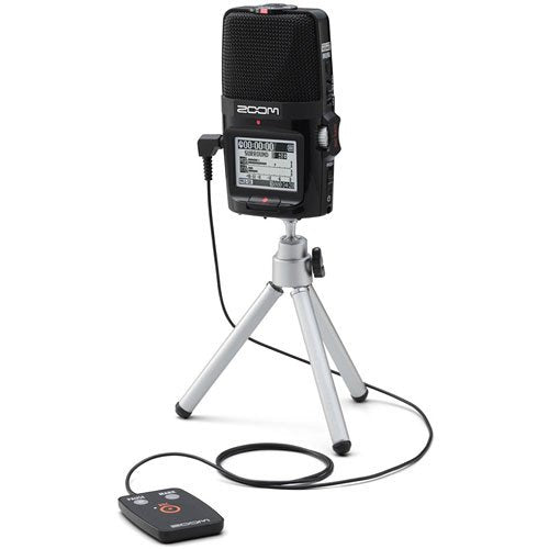 A Zoom H2n Handy Recorder mounted on a small tripod stand, with a wired remote control connected to it. The recorder's LCD screen displays recording information and audio levels