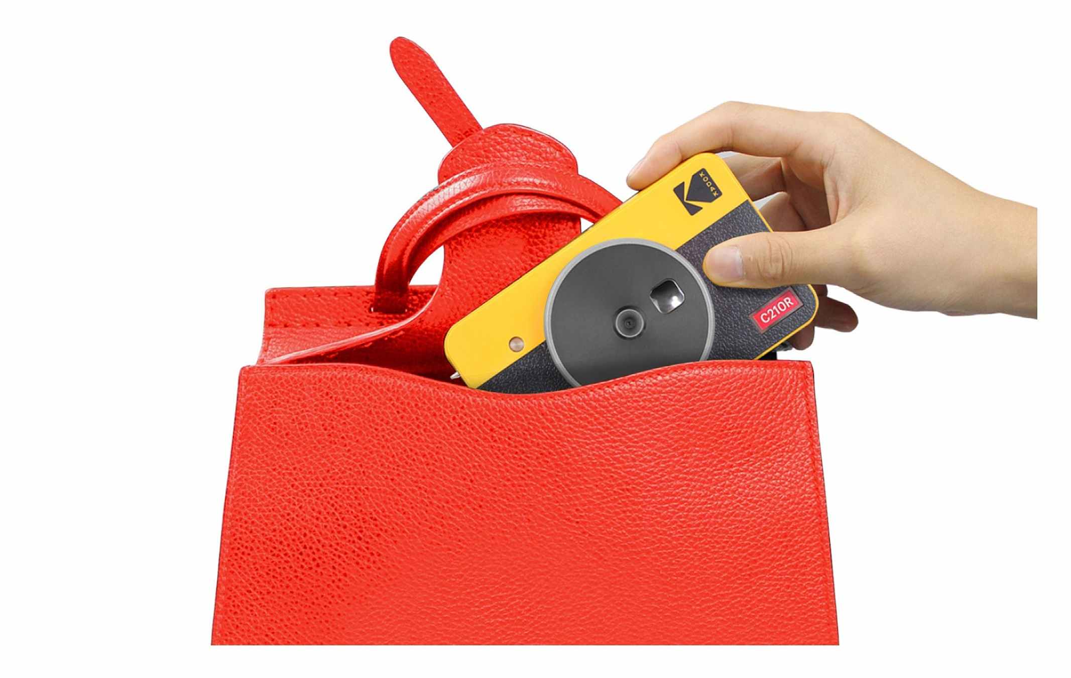 Kodak C210R instant camera in a compact yellow and black design, being placed into a stylish red handbag. The image highlights the camera’s portability and convenience for on-the-go use.